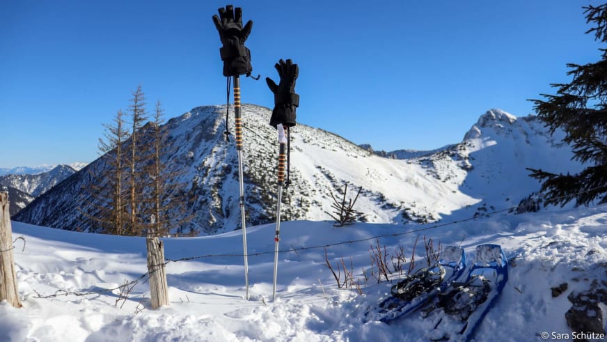 Trekkingstöcke mit Winterhandschuhen im Schnee vor Bergpanorama beim Schneeschuhwandern am Spitzingsee.