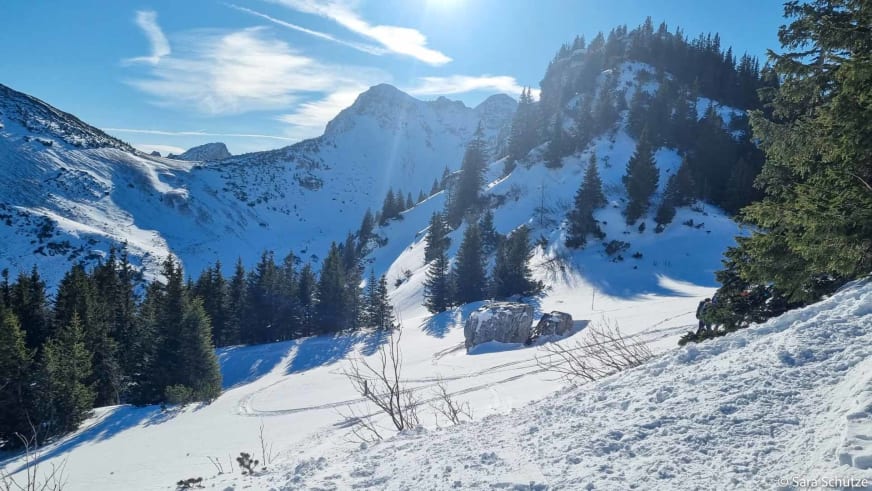 Schneeschuhtour am Spitzingsee: Schneeschuhwanderer in verschneitem Bergkessel vor markantem Felsengipfel im Gegenlicht.