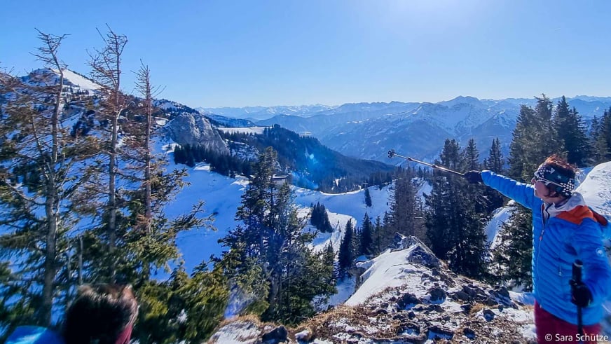 Schneeschuhwanderer zeigt vom Gipfel auf das Bergpanorama beim Schneeschuhwandern am Spitzingsee im Winter.