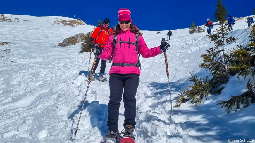 Schneeschuhwanderin in pinker Jacke mit Teleskopstöcken beim Abstieg auf verschneitem Hang am Spitzingsee