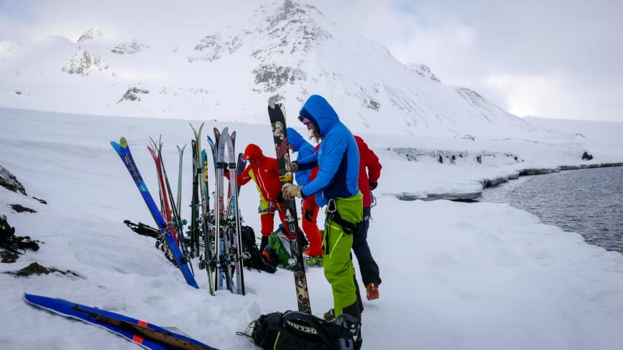 Skitour auf Spitzbergen: Skitourengeher bereiten Tourenski nach der Anlandung im Schnee vor verschneiten Bergen vor.
