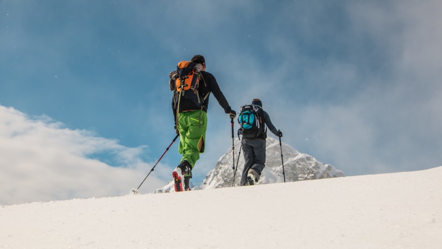 Zwei Skitourengeher steigen mit Fellen in Richtung des felsigen Gipfels Tafeltinden in Norwegen auf.