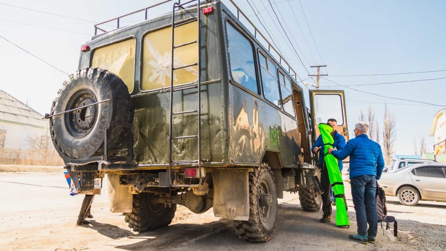 Skitour in Kirgistan: Skitourengeher verladen Ausrüstung an einem olivgrünen Allrad-LKW in einer Ortschaft.