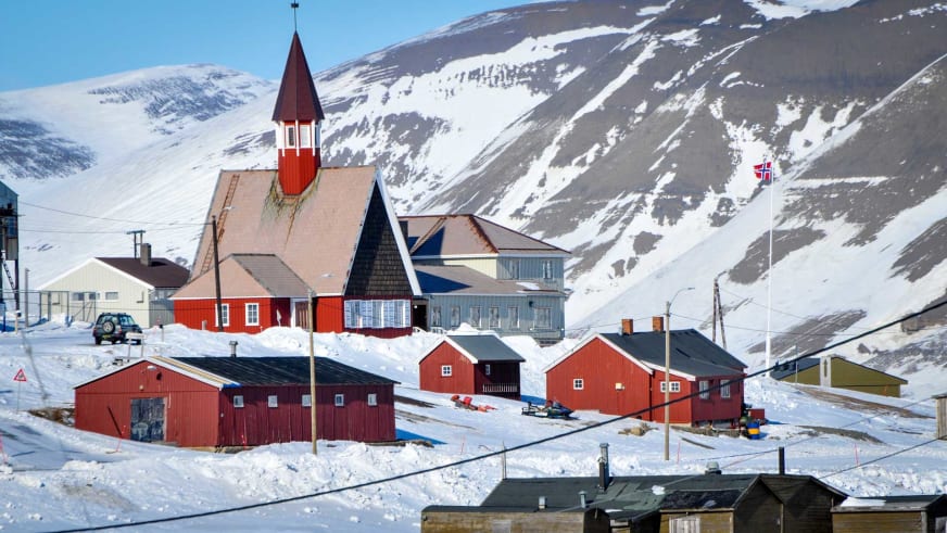 Skitour-Ausgangspunkt Longyearbyen: Rote Holzkirche mit Kirchturm im winterlichen Ort vor schneebedecktem Berg.