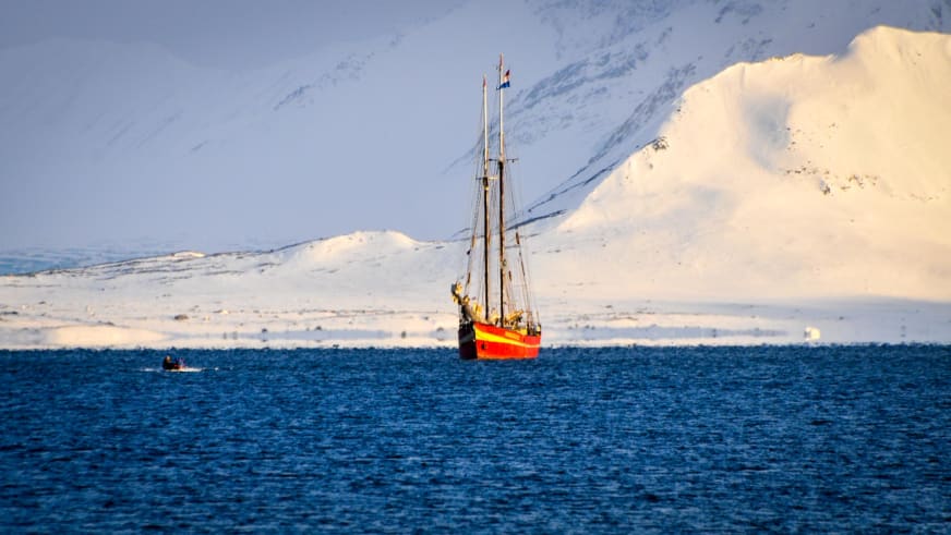 Skitour Spitzbergen: Segelschiff Noorderlicht mit rotem Rumpf vor schneebedeckter Bergkulisse auf Spitzbergen.