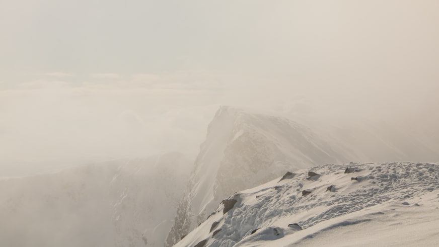 Skitour in den Lyngenalpen: verschneiter Felsgrat mit dunklen Felsblöcken und nebliger Bergkulisse bei diffusem Winterlicht