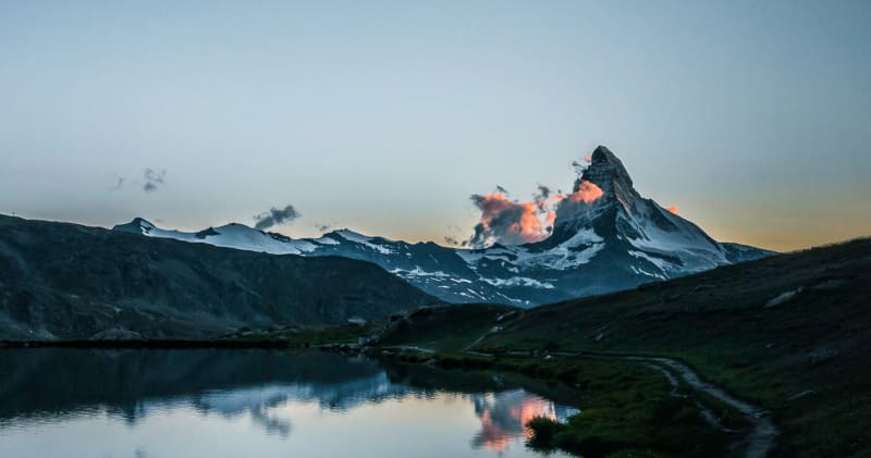 Bergwanderung am Matterhorn im Wallis: Bergsee spiegelt Dämmerungshimmel, pyramidenförmiger Gipfel im Hintergrund.
