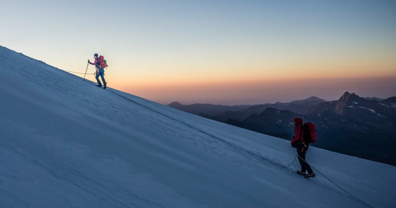Drei Bergsteiger in Seilschaft steigen bei Morgendämmerung den Firn hang der Spaghettirunde im Monte-Rosa-Massiv auf.