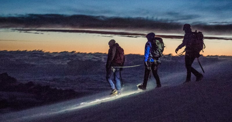 Hochtour auf die Signalkuppe im Wallis: drei Bergsteiger als Seilschaft steigen mit Steigeisen im Dämmerlicht auf.