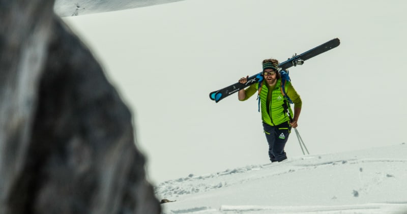 Einsteiger-Skitour: Person trägt Ski auf der Schulter und steigt einen steilen, schneebedeckten Hang im Skitourenkurs