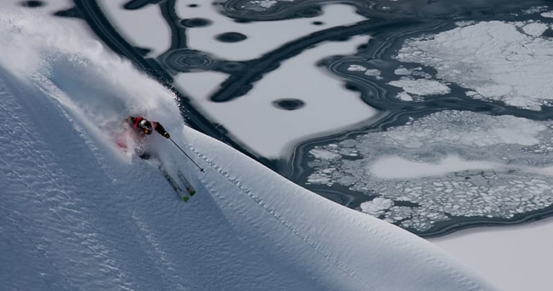 Skitourengeher fährt beim Freeriden einen steilen Tiefschneehang neben offenem Wasser mit Eisschollen ab.