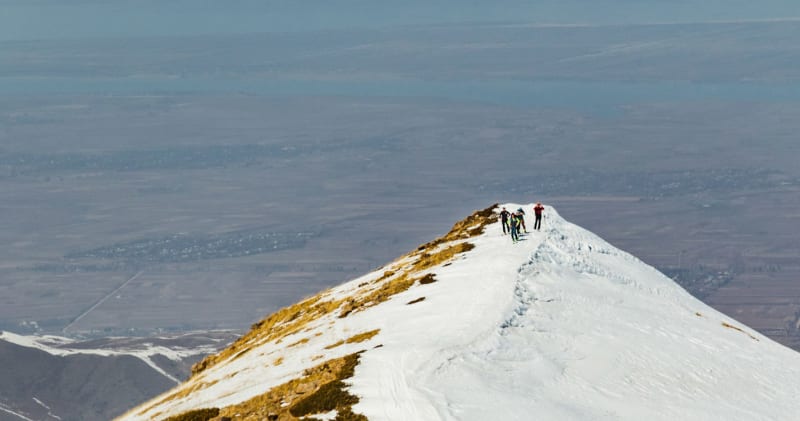 Vier Skitourengeher pausieren auf einem schneebedeckten Berggrat in Kirgisistan mit Talblick.