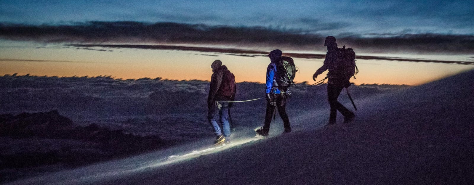 Hochtour auf die Signalkuppe im Wallis: drei Bergsteiger als Seilschaft steigen mit Steigeisen im Dämmerlicht auf.