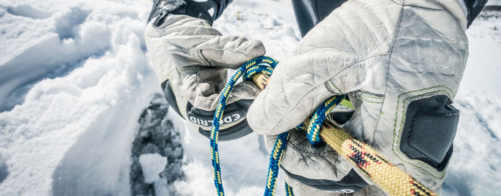 Bergtour Gletscherkurse für Einsteiger: Hände mit Winterhandschuhen führen zwei Kletterseile durch ein Edelrid-Sicherungsgerät