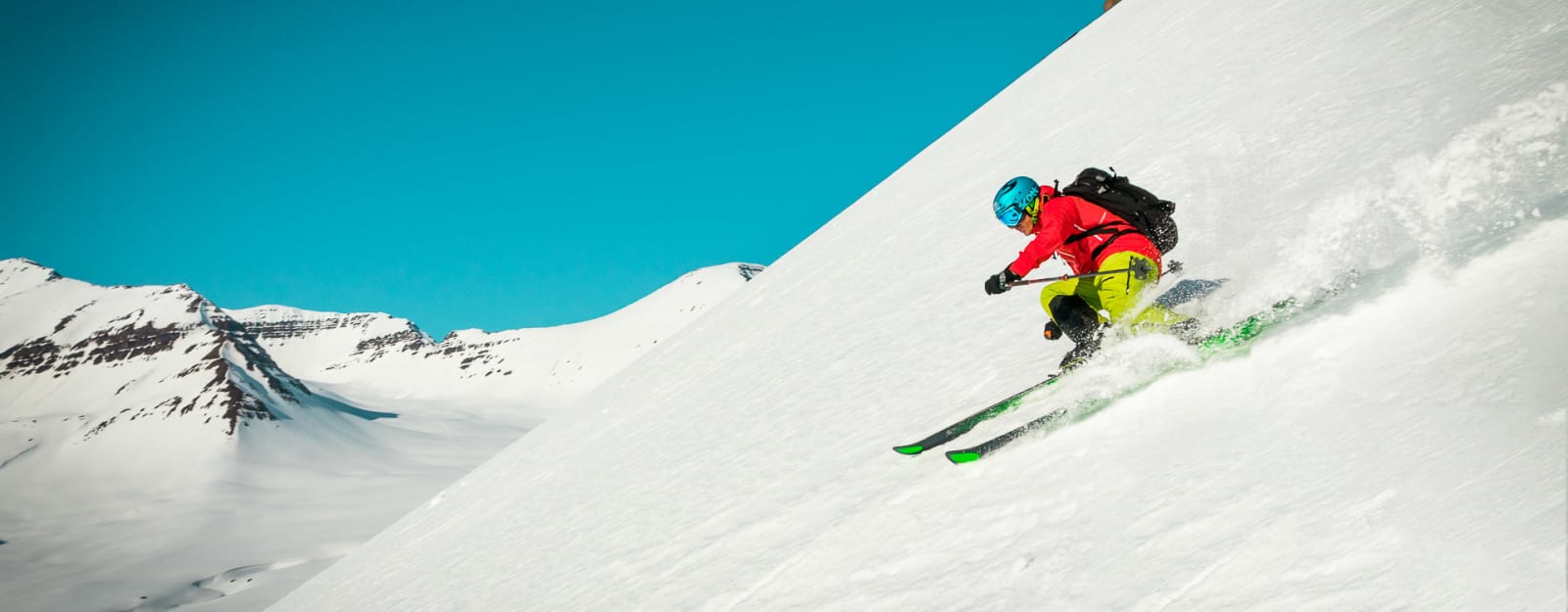 Skitourengeher fährt auf steilem Hang in Island mit Schneewolke unter den Ski ab.
