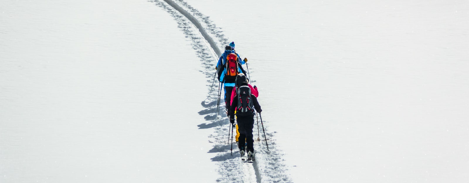 Drei Teilnehmer beim Skitourenkurs für Einsteiger steigen mit Fellen auf schneebedecktem Hang auf – Lawinenkurs inklusive.