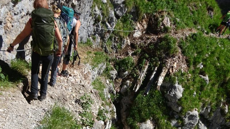Bergwanderer passieren einen gesicherten Felssteig mit Stahlseil auf dem Weg von der Gotzenalm zur Wasseralm.