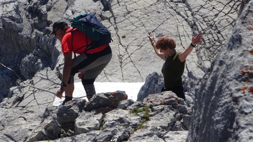 Zwei Personen bei der Bergwanderung im felsigen Anstieg zum Watzmann, klettern über hellen Kalkfels bei Sonnenschein.