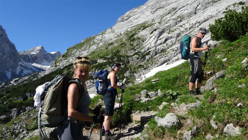 Drei Personen mit Rucksäcken und Wanderstöcken bei der Bergwanderung auf dem steinigen Aufstieg zum Watzmannhaus.