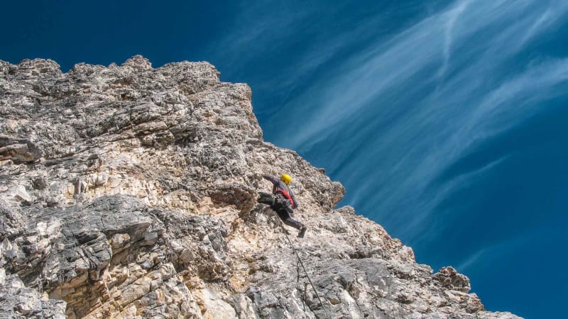 Kletterer mit gelbem Helm und Gurt in einer steilen Kalkfelswand in den Dolomiten, Froschperspektive