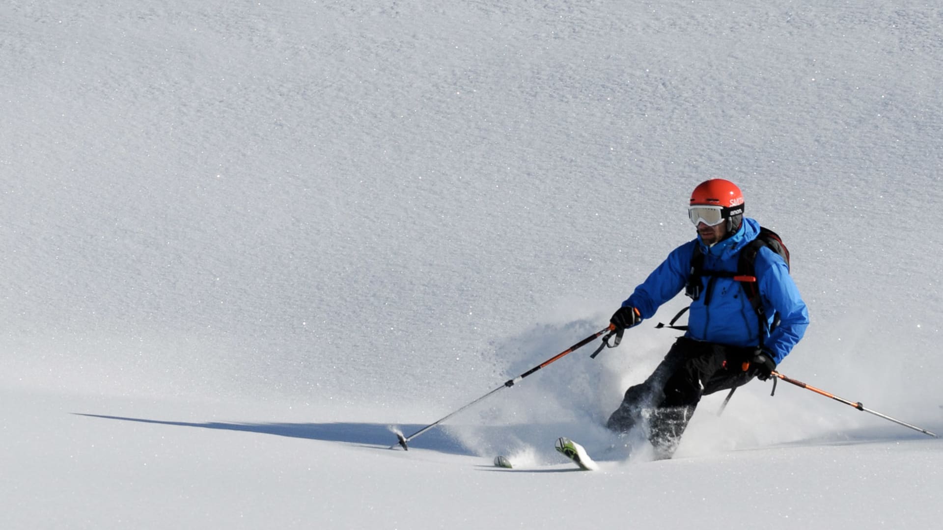 Skitouren-Fahrer in blauer Jacke beim Tiefschneefahren am Pitztaler Gletscher, mit aufwirbelnder Pulverschneewolke