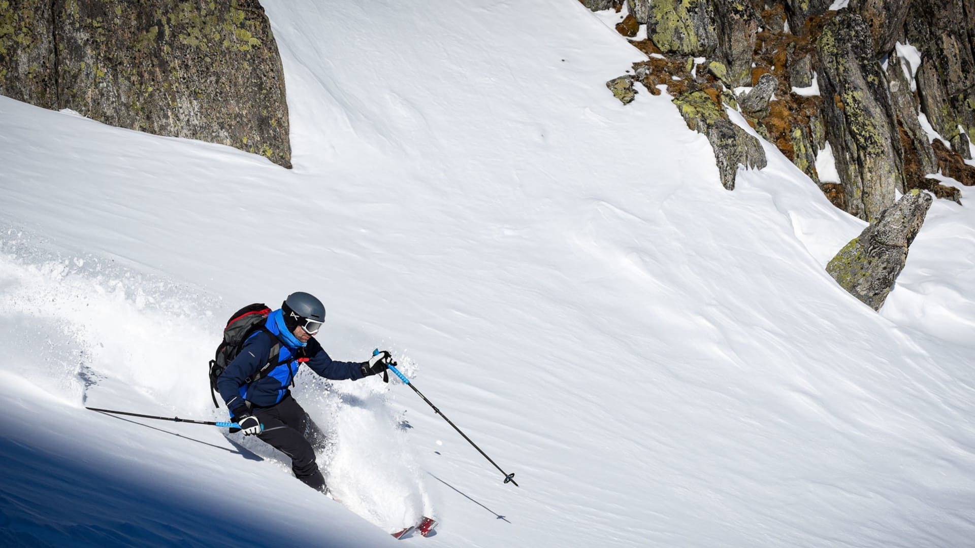 Skitourengeher übt Tiefschneetechnik in Kurvenfahrt vor Felsformationen auf Skitour bei Disentis.
