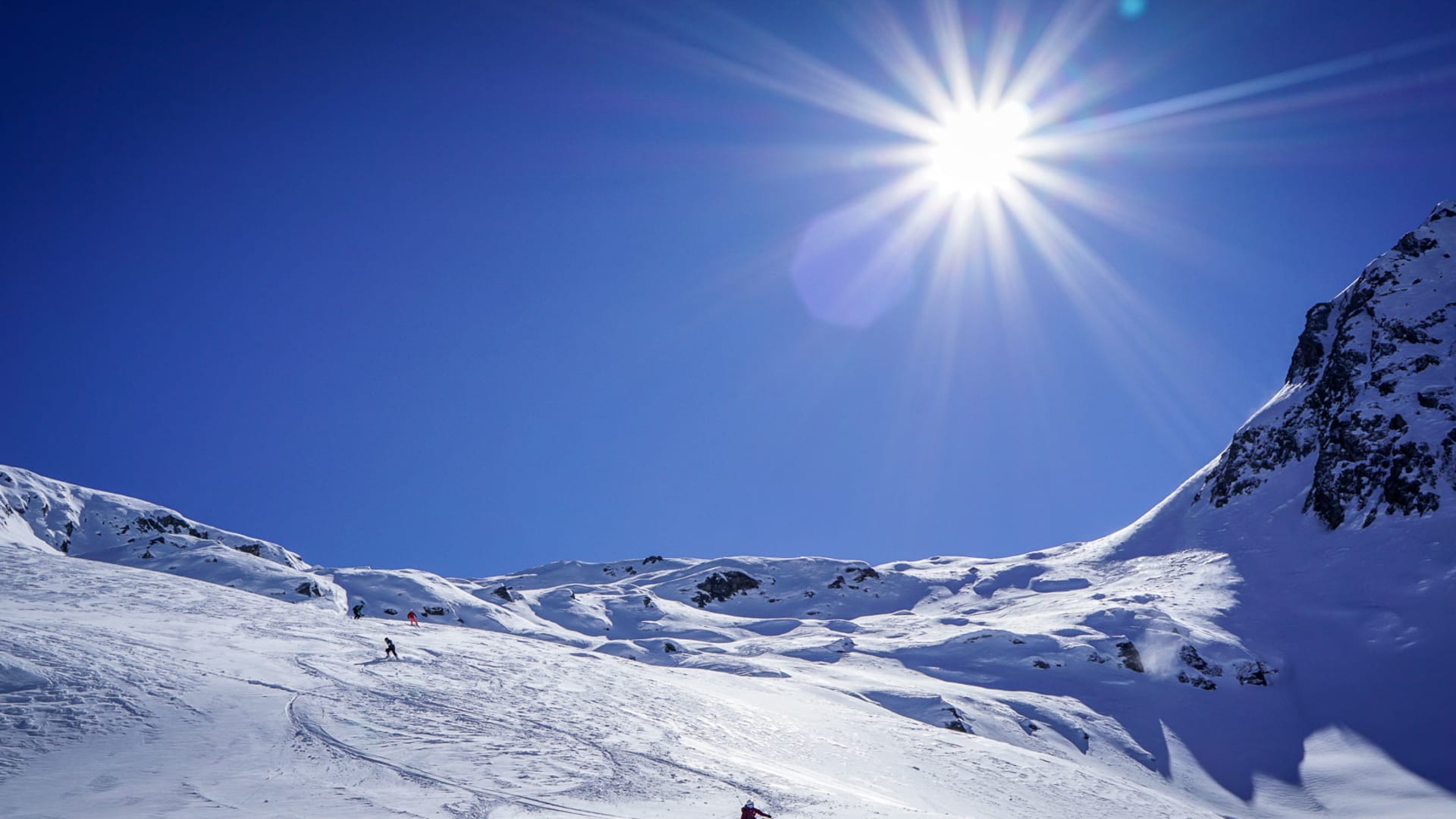 Vier Skitourengeher fahren Skifahrspuren in einem schneebedeckten Hochgebirgskessel bei Disentis ab.
