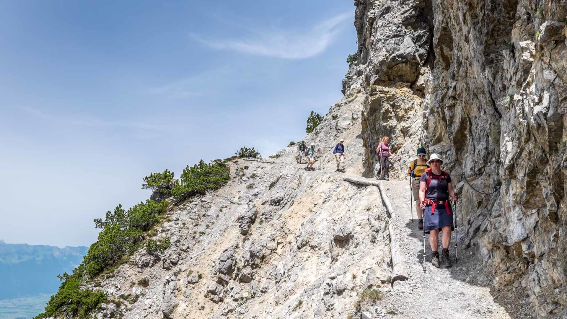 Bergwanderergruppe traversiert einen in Kalkfels gehauenen, mit Stahlseil gesicherten Steig in Liechtenstein.