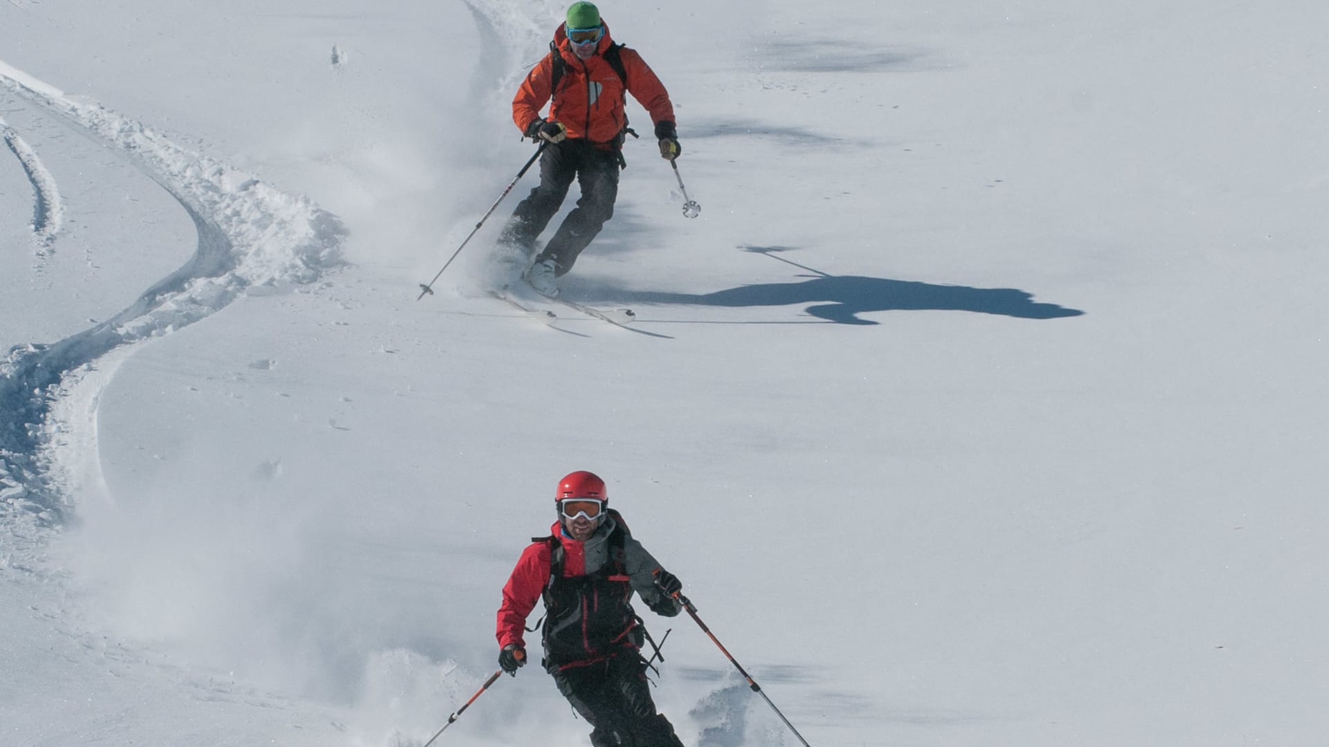Zwei Skitourengeher fahren mit Schneestäubern einen Tiefschnee-Hang ab, Skitour Disentis.