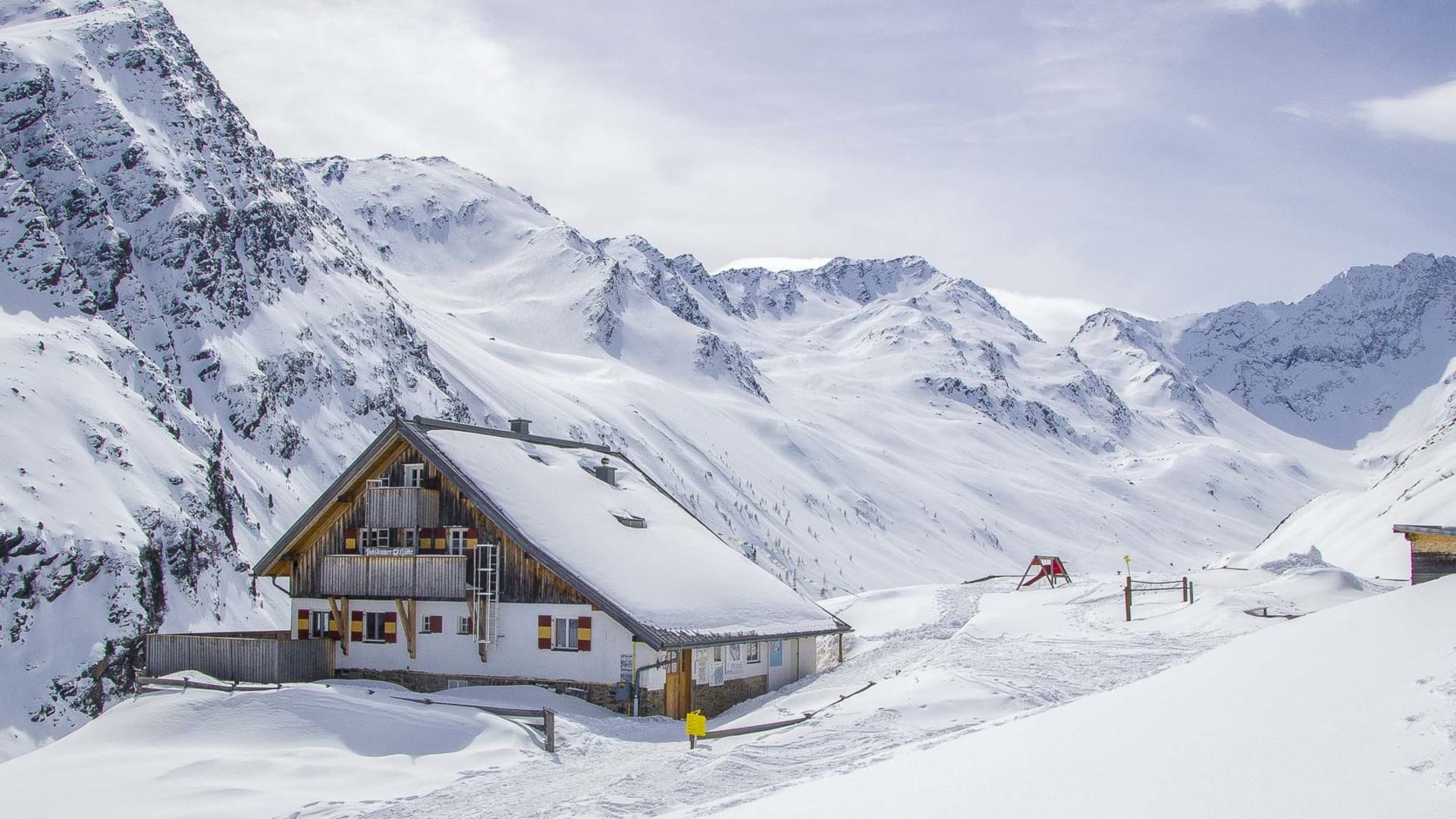 Potsdamer Hütte im Sellrain: zweigeschossiges Alpengasthaus mit rotem Fensterladen und Schneeauflage im Gebirgstal.