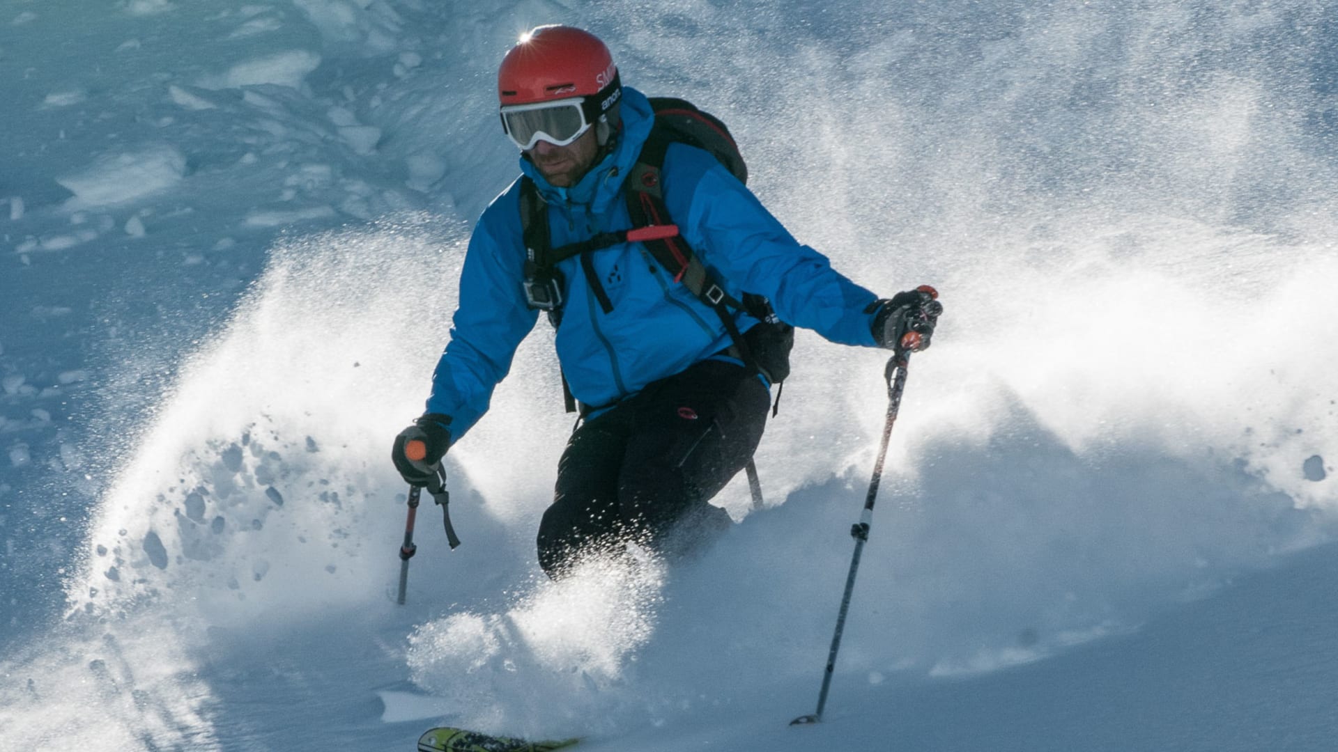 Freerider in blauer Skijacke und rotem Helm fährt mit Pulverschneewolke auf Freeride-Gelände in Disentis.