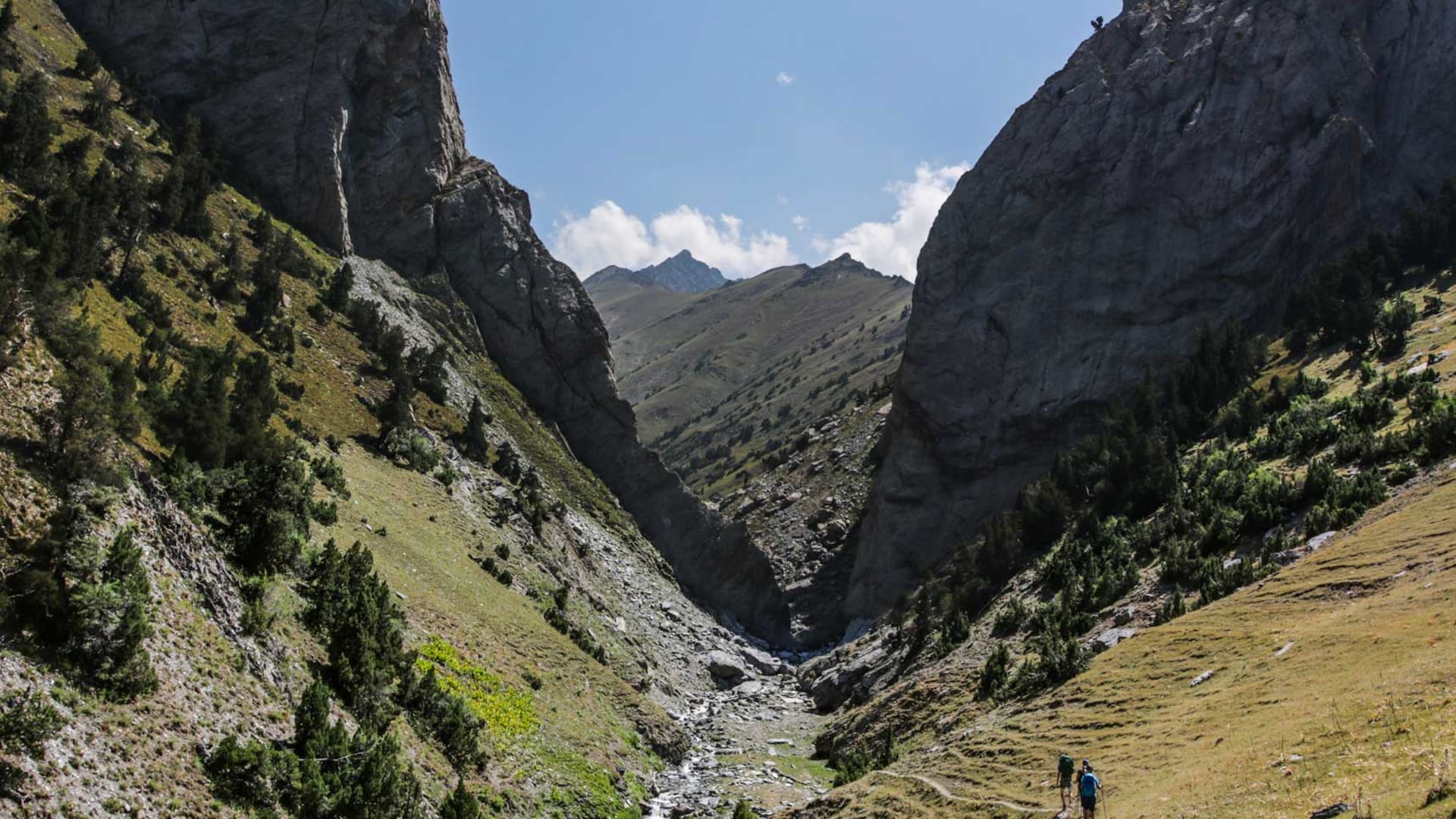 Zwei Trekker wandern auf einem Hangpfad in eine felsige Bergschlucht in Kirgistan.