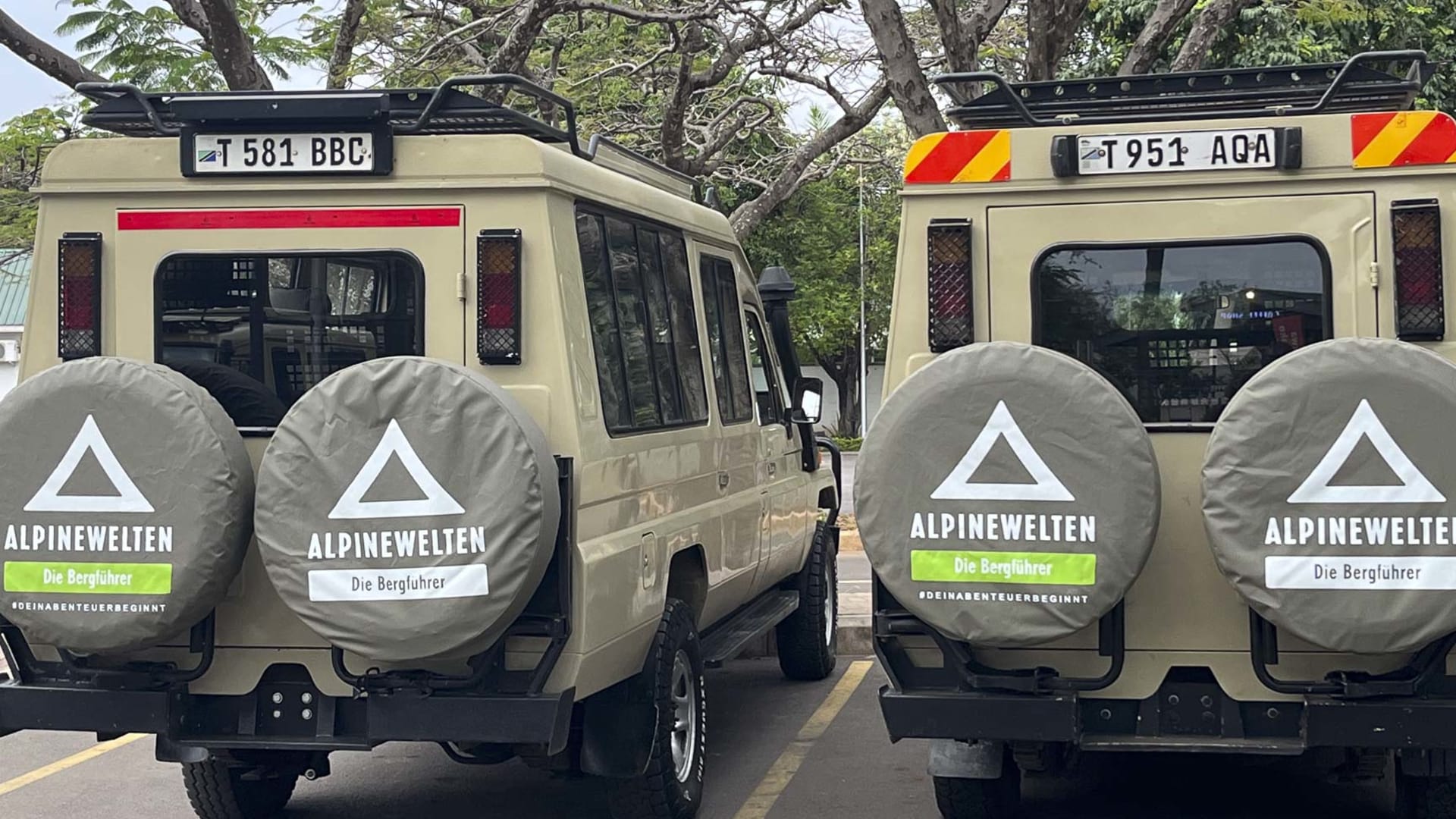 Zwei beige Toyota-Geländefahrzeuge mit Alpinewelten-Logo stehen auf einem Parkplatz in Tansania.