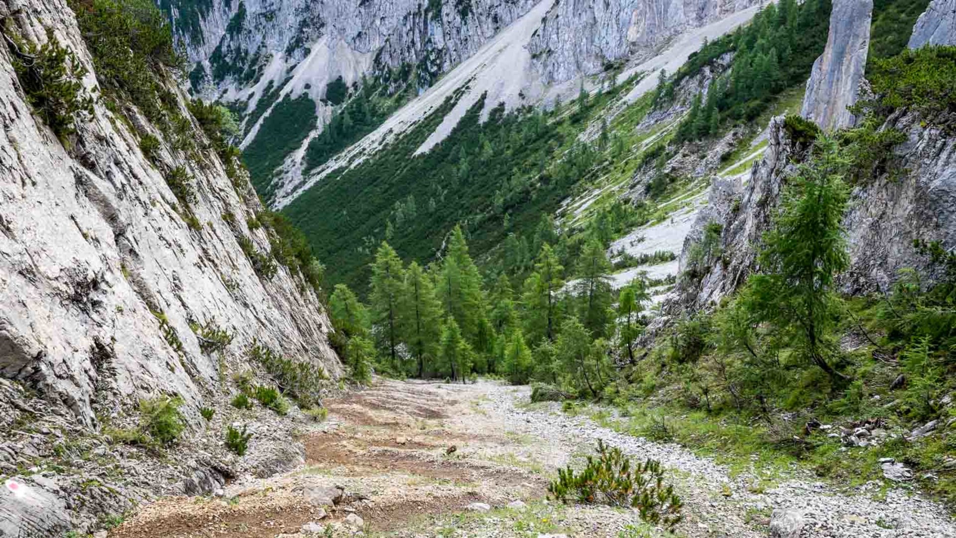 Breiter Schutt- und Geröllweg zieht sich durch eine enge Felsschlucht im Karwendel, mit roter Wegmarkierung am Stein.