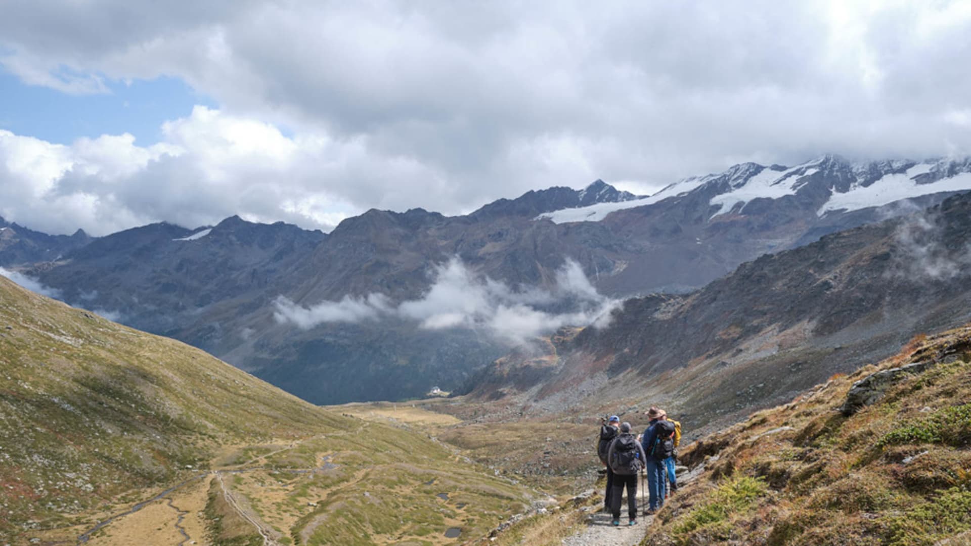 Bergwanderung auf dem Höhenweg: drei Bergwanderer mit Rucksäcken blicken ins alpine Hochtal der Ortlergruppe.