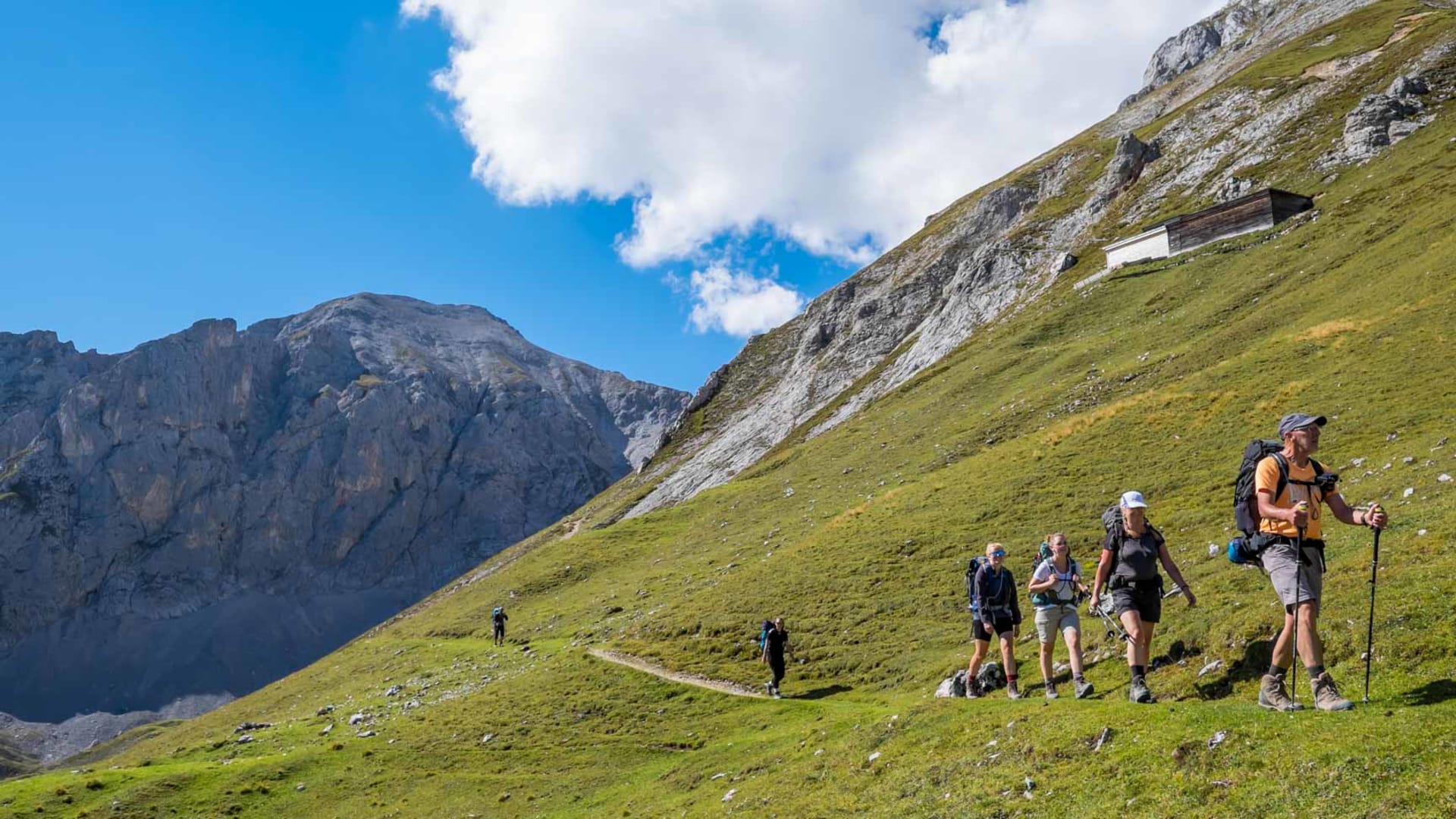 Gruppe bei der Bergwanderung am Hohen Dachstein auf einem Almweg mit Almhütte und felsiger Bergwand im Hintergrund.