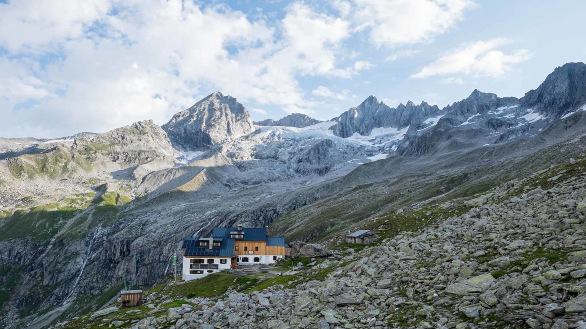 Bergwanderung im Zillertal: Plauener Hütte mit weißer Fassade und Solarpaneelen vor grauem Gletscher und Felsgraten.