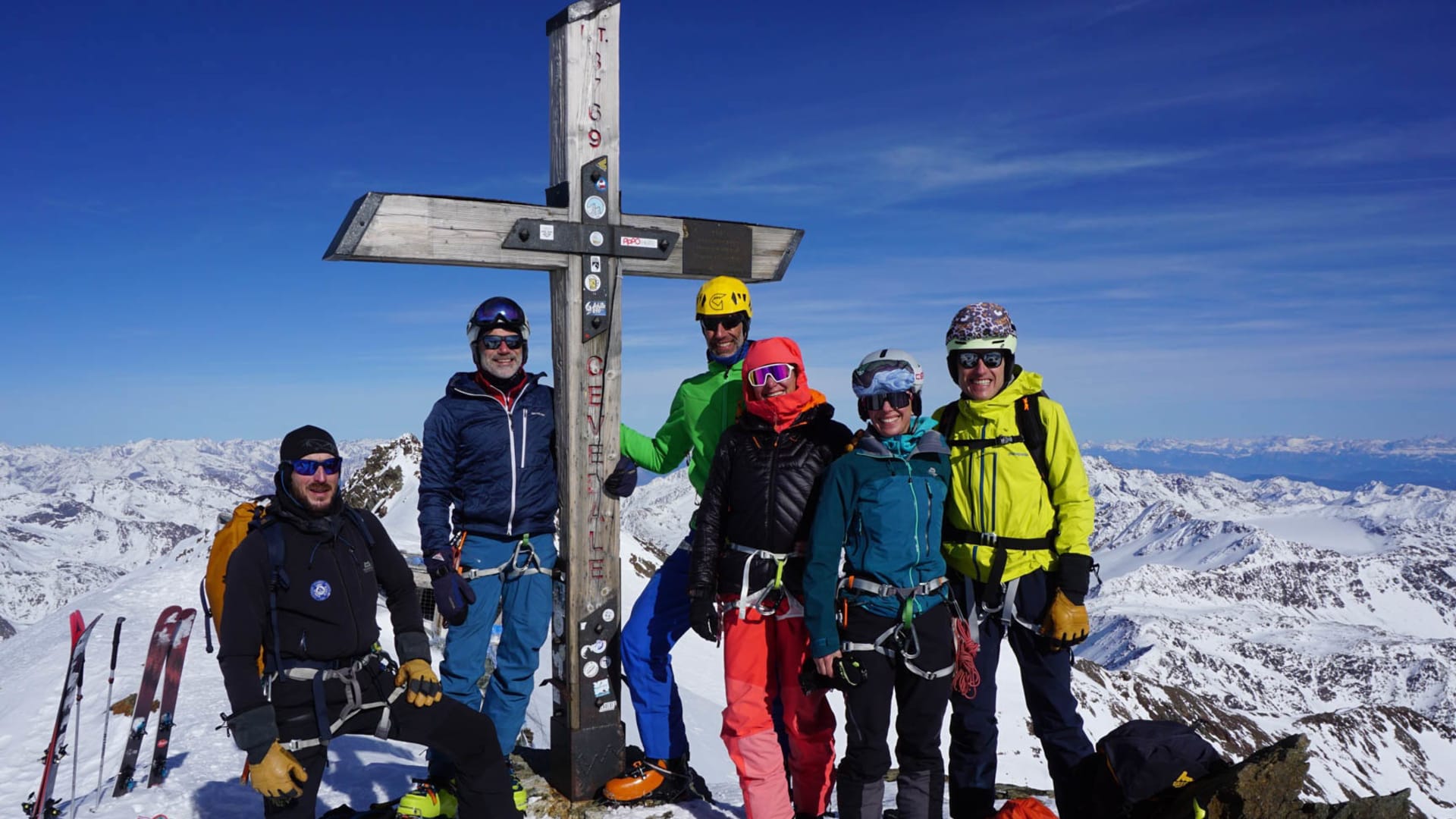 Fünf Skitourengeher posieren am Gipfelkreuz des Cevedale vor einem Hochgebirgspanorama.