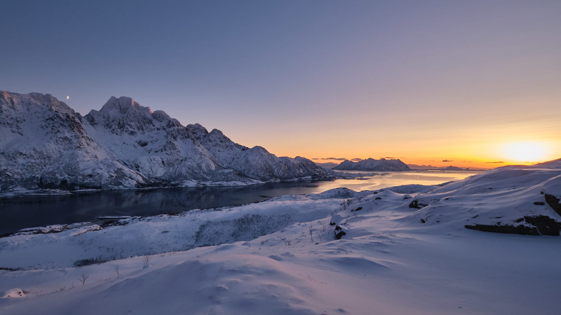 Winterwanderung auf den Lofoten: schneebedeckte Fjordlandschaft mit felsigen Gipfeln, Mondsichel