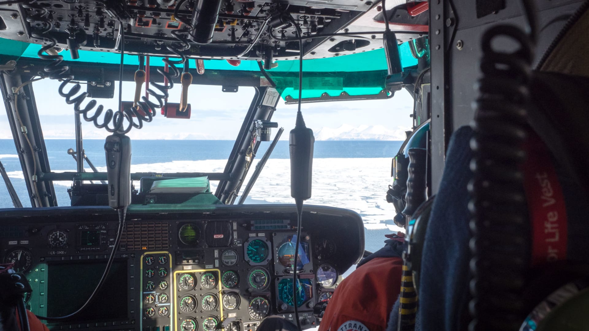 Cockpit eines SAR Helicopter LN-OMX mit Pilot in roter Lufttransport-Jacke, Headset und Instrumentenpanel
