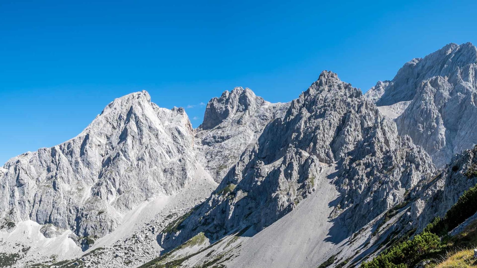 Panoramablick auf die Kalkgipfel des Dachsteinmassivs bei der Bergwanderung: helle Felswände, Geröllhang und Latschenkiefern