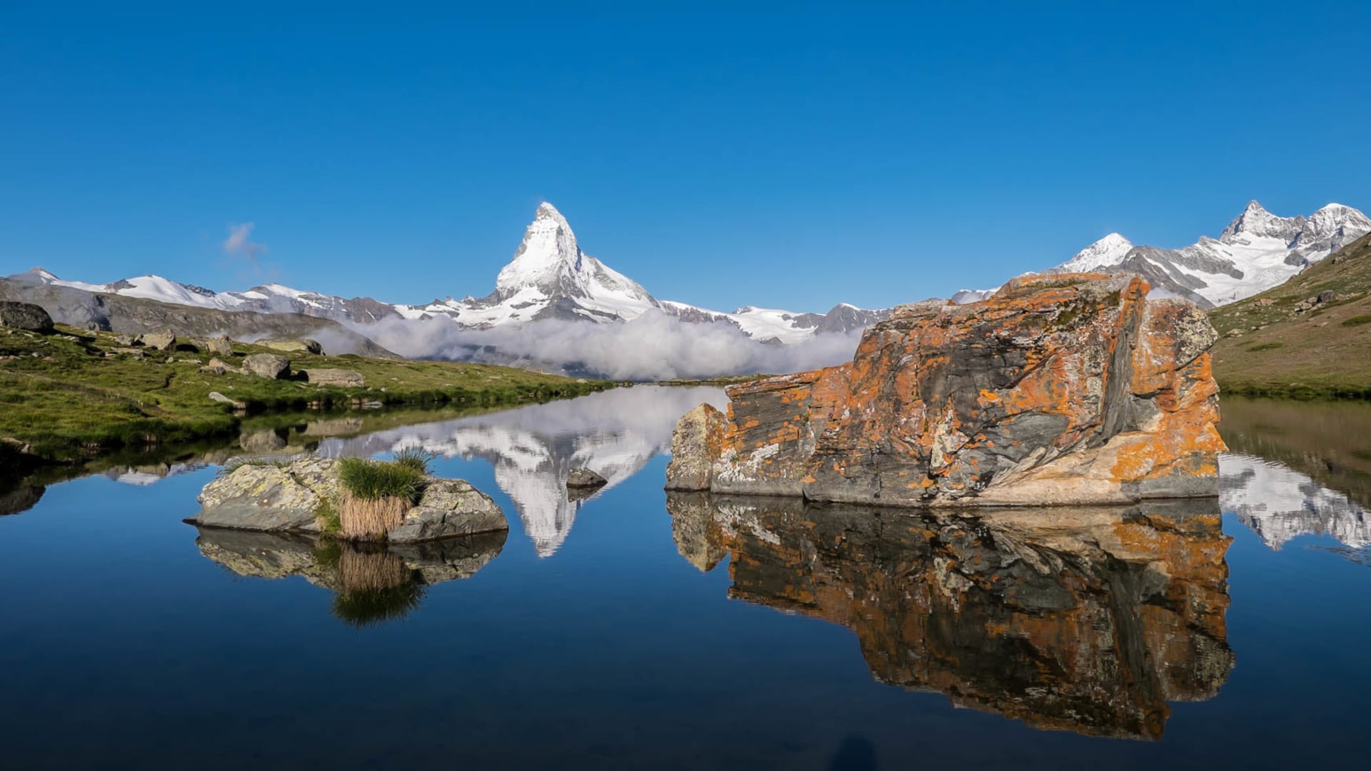 Bergwanderung am Matterhorn: Hochgebirgssee spiegelt den pyramidenförmigen Gipfel mit Gletschern und Wolkenbank im Sommer