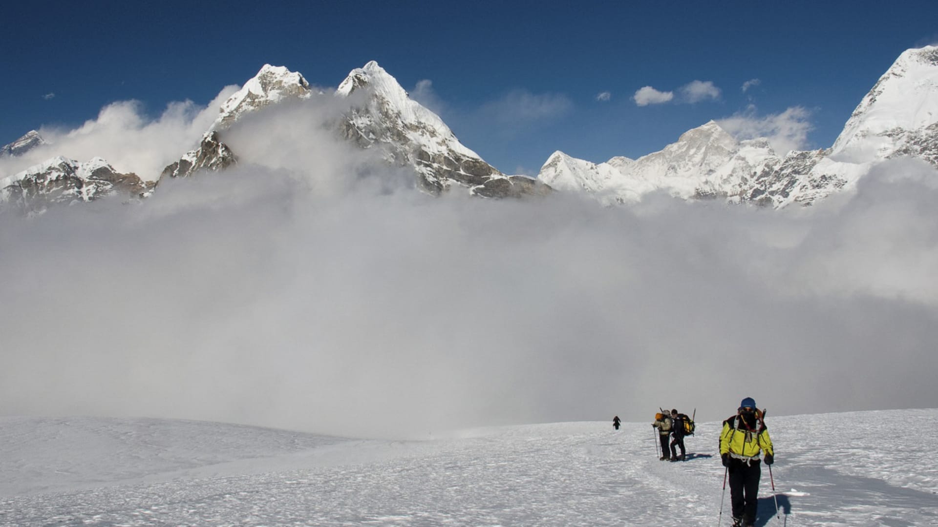 Vier Höhenbergsteiger steigen mit Trekkingstöcken in einer Linie über ein Schneeplateau zum Mera Peak auf.