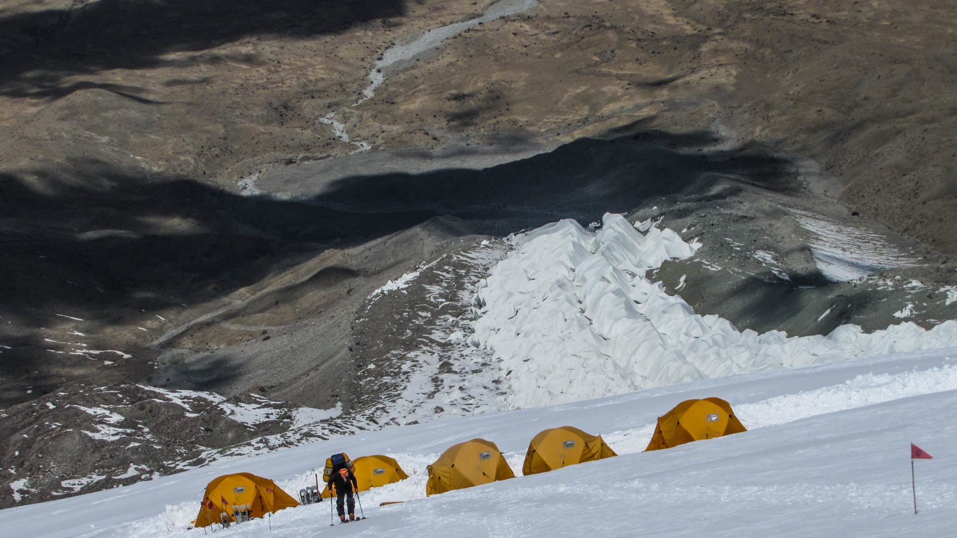 Expedition zum Muztagata: Hochlager mit fünf Zelten, ein Höhenbergsteiger mit Rucksack und Steigeisen steigt den Schneehang auf.
