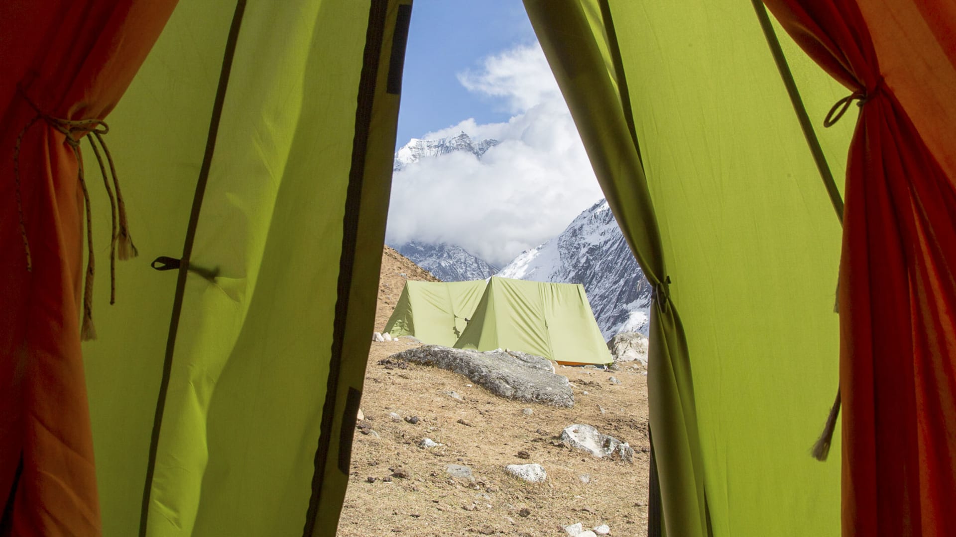 Expedition am Manaslu: Blick aus geöffnetem Zelt auf das Basislager mit weiteren Zelten und schneebedeckten Gipfeln.