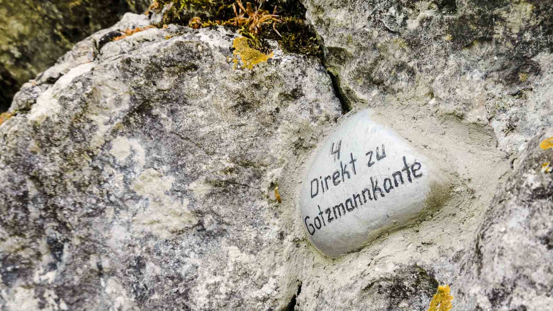 Klettern im Donautal: beschrifteter Kieselstein mit Routenhinweis zur Gotzmannkante zwischen grauen Kalkfelsblöcken mit Flechten.