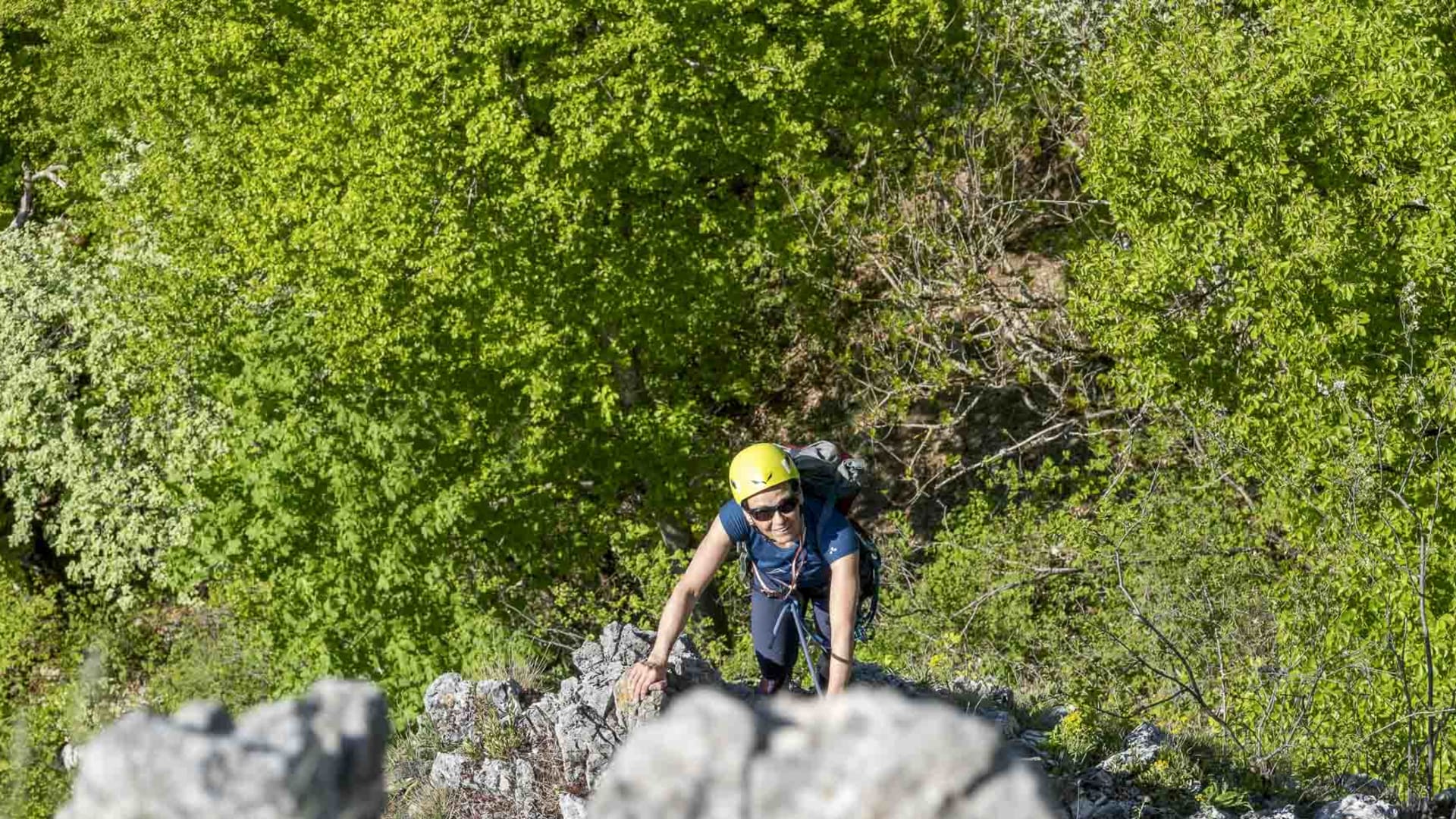 Kletterer mit gelbem Helm und Rucksack steigt am hellen Kalksteingrat im Donautal aufwärts, Seil gesichert.