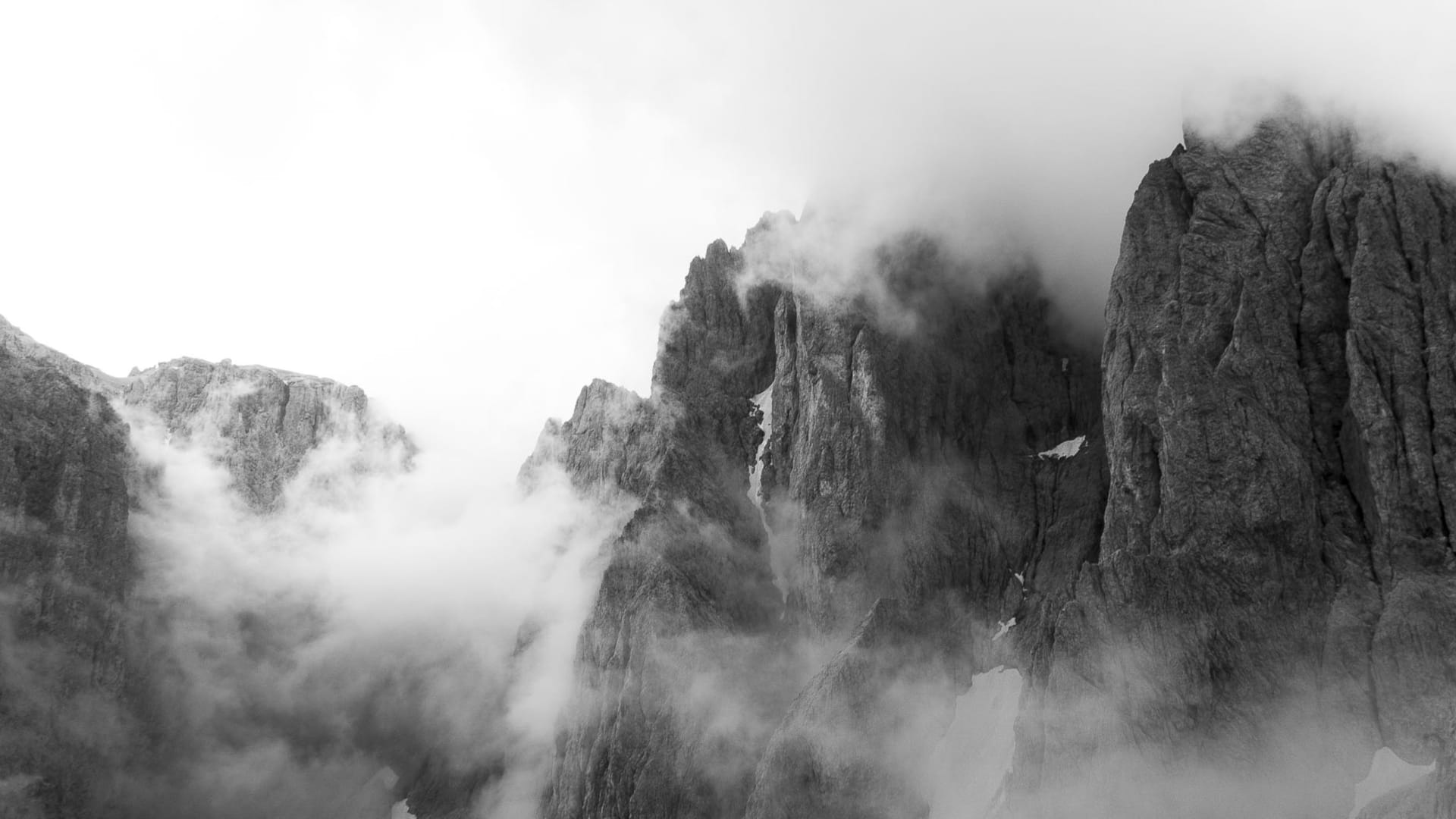 Schwarzweißpanorama zerklüfteter Felstürme und Grate am Sella in den Dolomiten, umhüllt von Nebelschwaden und Wolken.