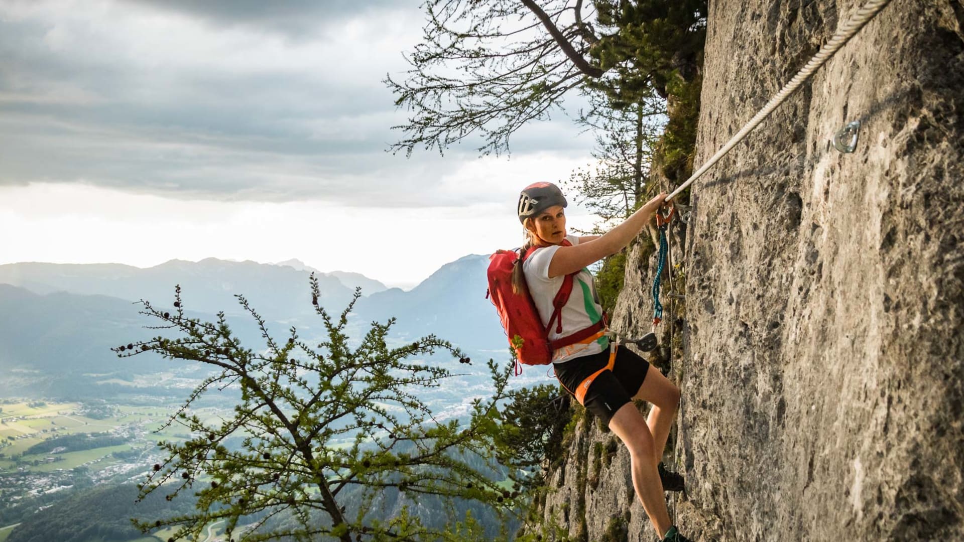 Klettersteiggeherin klettert am Laxersteig am Jenner an senkrechter Kalkwand mit Talblick.