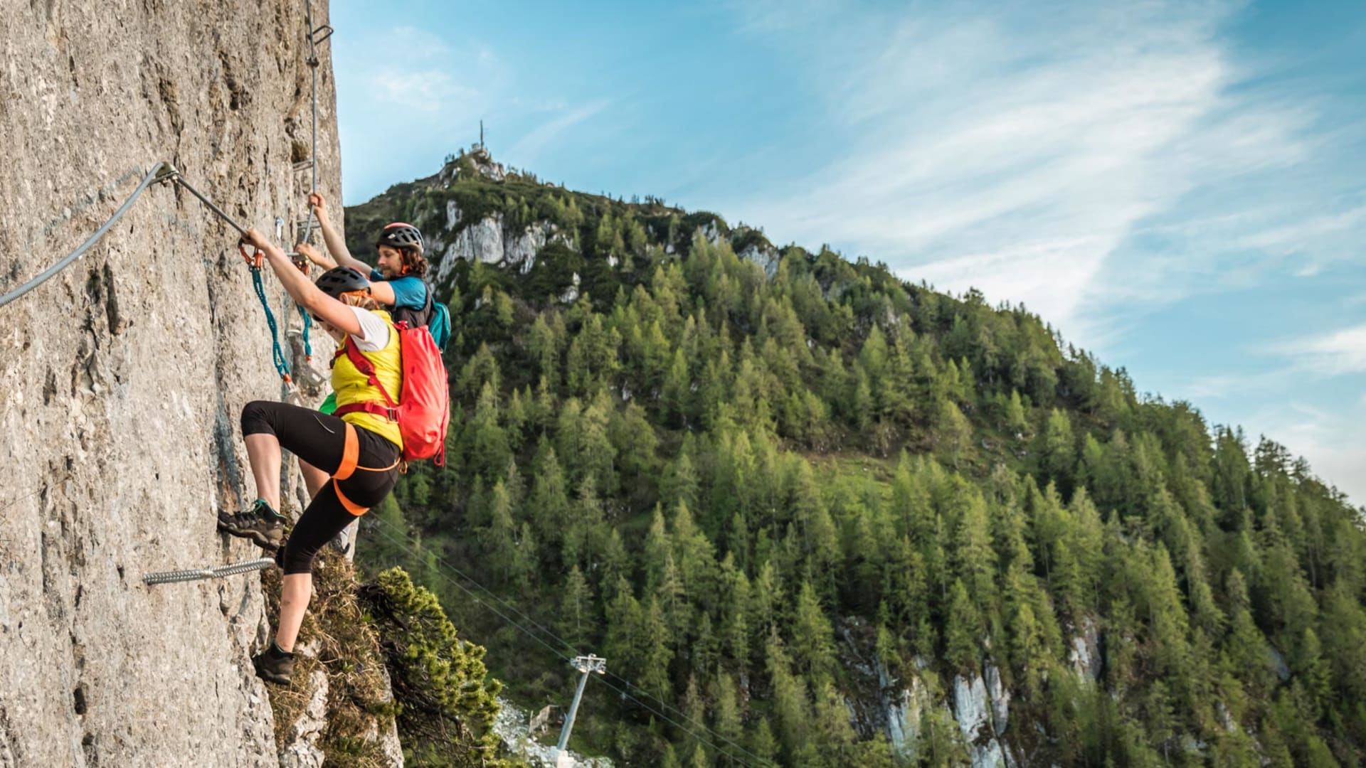Zwei Klettersteiggeher sichern sich am Drahtseil einer senkrechten Passage des Jenner Laxersteigs.